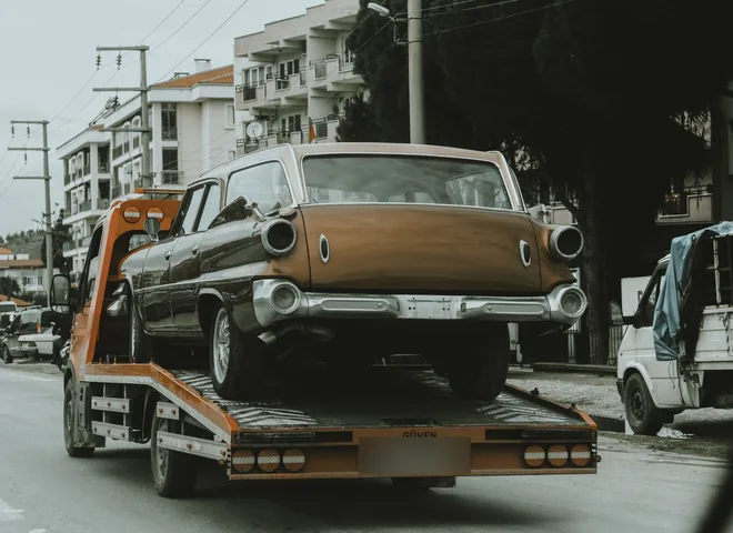 Vintage car being transported on a flatbed tow truck through the city
