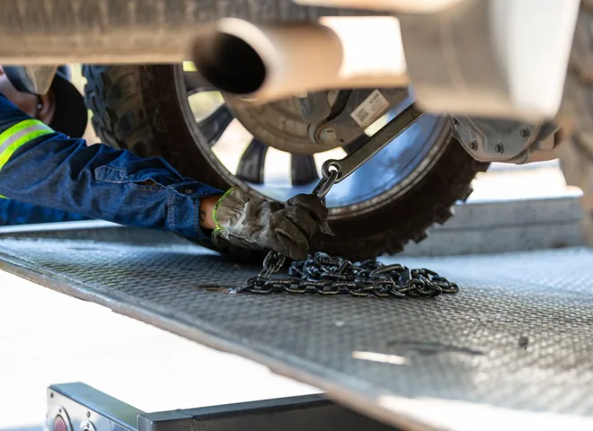 Operator securing a car wheel with chains on a tow truck platform