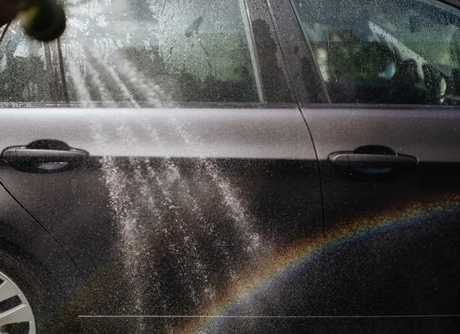 Pressure-washer spray rinsing the side of a dark car